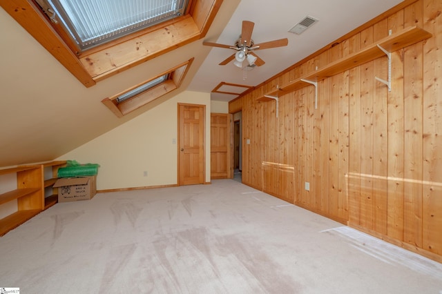 additional living space featuring carpet, visible vents, lofted ceiling with skylight, a ceiling fan, and wooden walls