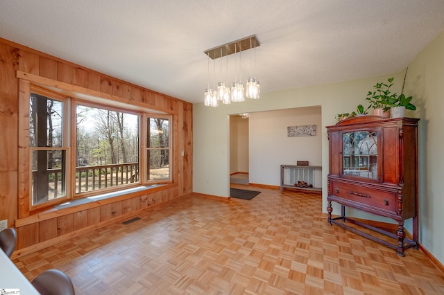 dining room featuring visible vents, wooden walls, baseboards, and a textured ceiling