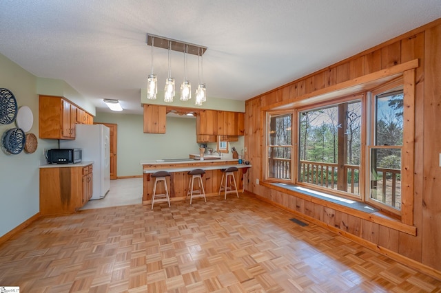 kitchen featuring a peninsula, wood walls, visible vents, and brown cabinets