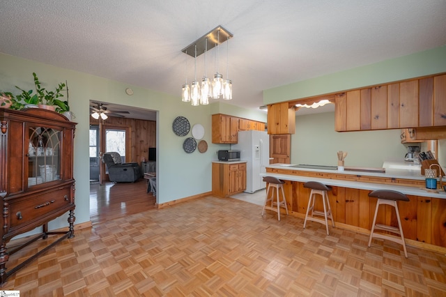 kitchen featuring a textured ceiling, white refrigerator with ice dispenser, light countertops, stainless steel microwave, and a kitchen bar