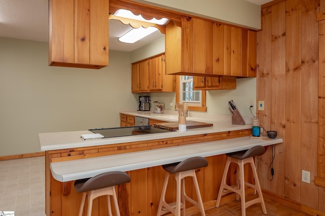 kitchen featuring a peninsula, a breakfast bar, brown cabinets, and light countertops