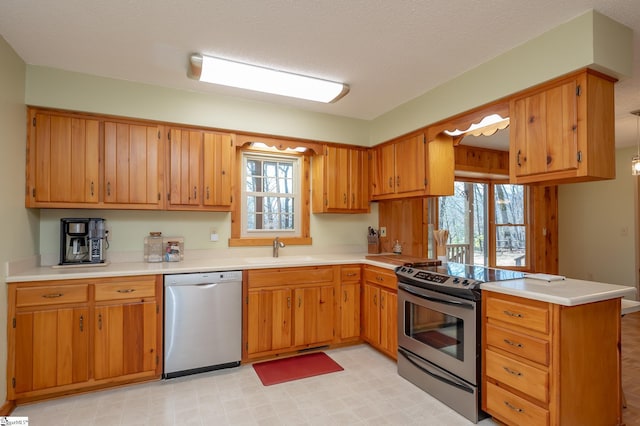 kitchen with stainless steel appliances, a peninsula, a sink, and light countertops