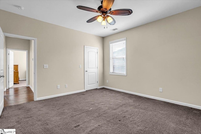 unfurnished bedroom featuring dark colored carpet, visible vents, baseboards, and a ceiling fan