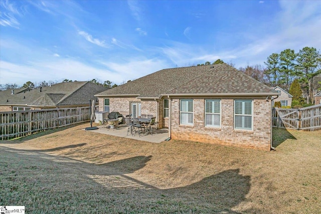 back of house with roof with shingles, a fenced backyard, a lawn, a patio area, and brick siding