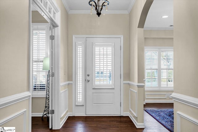 entryway with arched walkways, a notable chandelier, dark wood-style floors, and crown molding