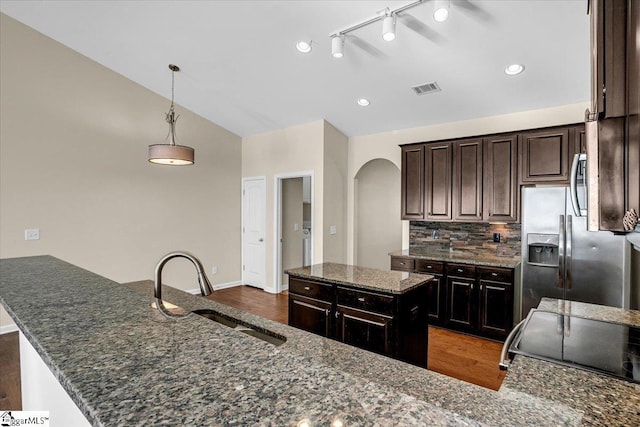 kitchen featuring visible vents, a sink, backsplash, arched walkways, and lofted ceiling