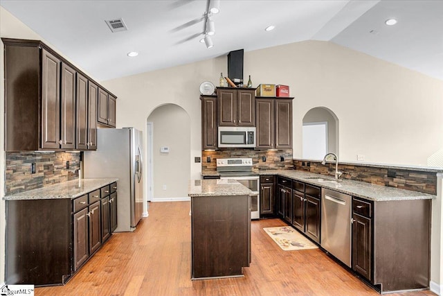 kitchen featuring a kitchen island, lofted ceiling, appliances with stainless steel finishes, arched walkways, and a sink