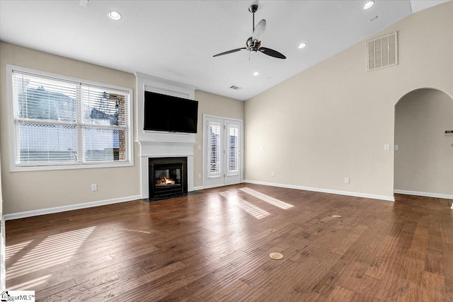 unfurnished living room with visible vents, ceiling fan, a fireplace with flush hearth, wood finished floors, and arched walkways