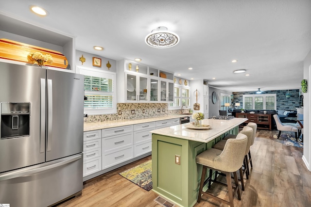 kitchen featuring a kitchen breakfast bar, white cabinets, stainless steel refrigerator with ice dispenser, light wood finished floors, and glass insert cabinets