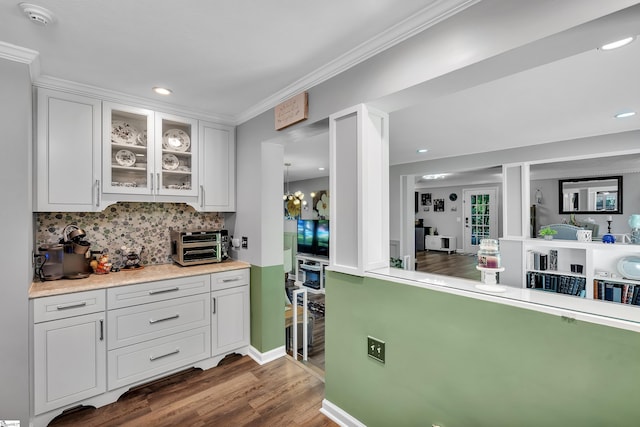 kitchen with tasteful backsplash, glass insert cabinets, ornamental molding, dark wood-type flooring, and white cabinetry