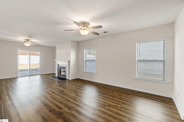 unfurnished living room featuring baseboards, visible vents, dark wood finished floors, and a glass covered fireplace