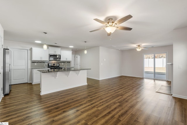 kitchen with a kitchen island with sink, stainless steel appliances, dark wood-style flooring, backsplash, and a kitchen bar