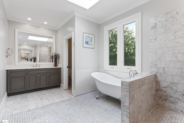 full bath with a skylight, crown molding, tile walls, a freestanding bath, and vanity