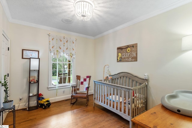 bedroom featuring a textured ceiling, wood finished floors, baseboards, ornamental molding, and a nursery area