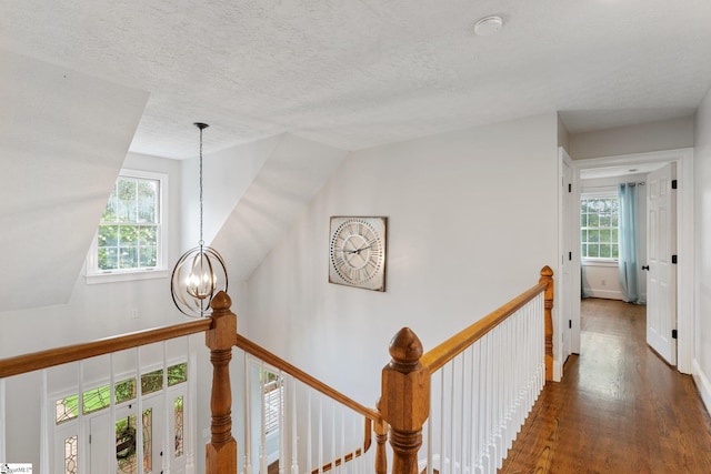 hall with a chandelier, a textured ceiling, an upstairs landing, and wood finished floors