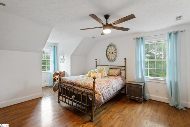 bedroom featuring visible vents, vaulted ceiling, a textured ceiling, and wood finished floors