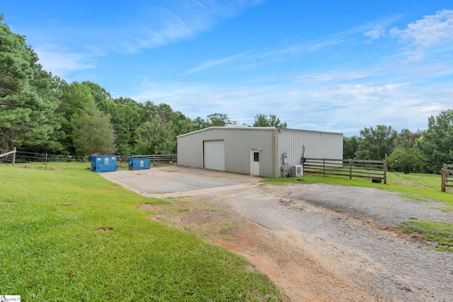 view of pole building featuring driveway, a rural view, fence, and a yard