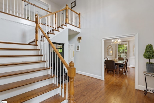 staircase with a towering ceiling, an inviting chandelier, baseboards, and wood finished floors