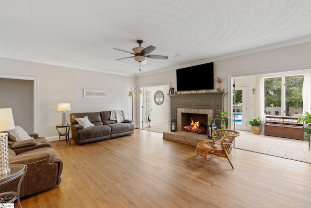 living area with crown molding, a fireplace, light wood finished floors, and a ceiling fan