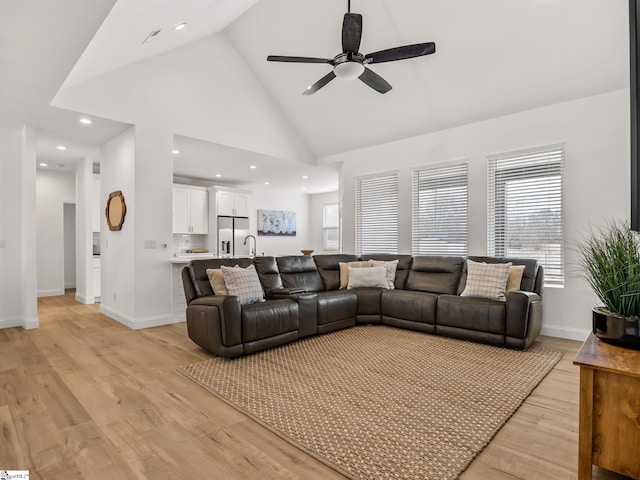 living room featuring high vaulted ceiling, baseboards, ceiling fan, and light wood finished floors