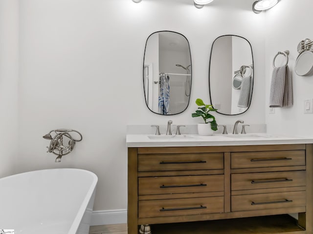 bathroom featuring double vanity, a freestanding bath, baseboards, and a sink