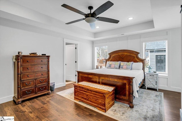 bedroom featuring wood finished floors, recessed lighting, a raised ceiling, and baseboards