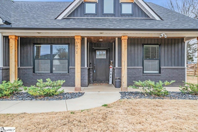 entrance to property with board and batten siding, covered porch, brick siding, and a shingled roof