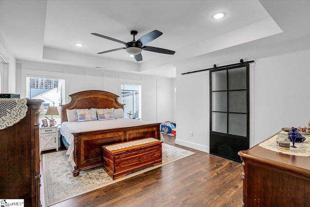 bedroom featuring a barn door, a ceiling fan, a raised ceiling, and wood finished floors