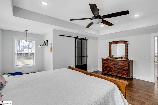 bedroom featuring recessed lighting, a raised ceiling, a barn door, wood finished floors, and baseboards