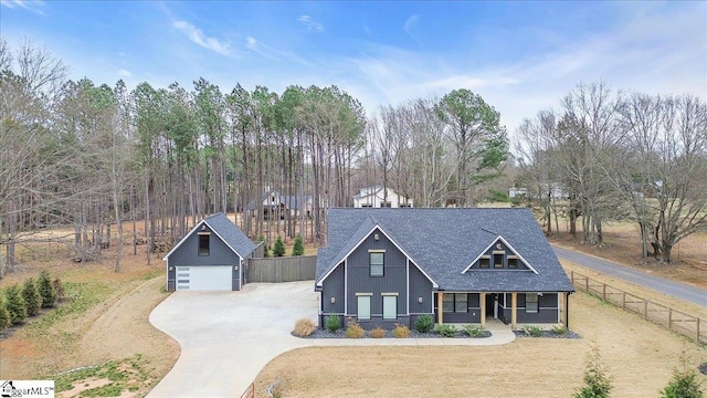 view of front of property featuring covered porch, a shingled roof, a detached garage, and fence