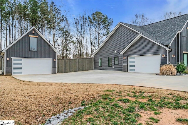 view of home's exterior featuring a shingled roof, concrete driveway, and fence