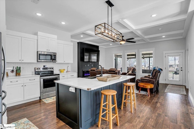 kitchen with appliances with stainless steel finishes, open floor plan, dark wood-style flooring, a sink, and backsplash