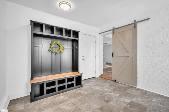 mudroom featuring brick wall, a barn door, and baseboards