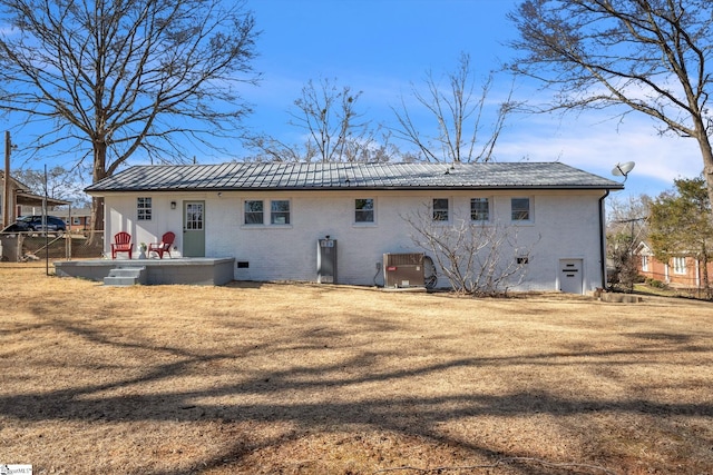 back of property featuring brick siding, a lawn, and central AC