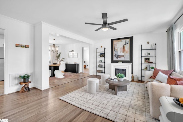 living room featuring ceiling fan with notable chandelier, visible vents, light wood-style floors, a glass covered fireplace, and crown molding