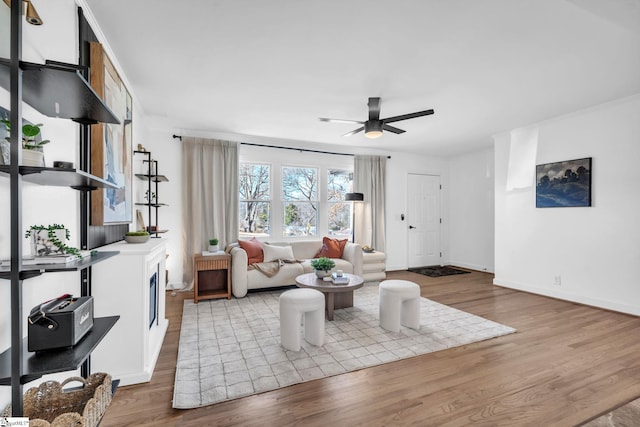 living room with ornamental molding, wood finished floors, a ceiling fan, and baseboards