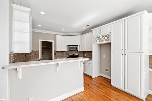 kitchen with appliances with stainless steel finishes, a breakfast bar area, light countertops, white cabinetry, and open shelves