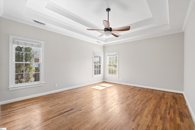 spare room with a tray ceiling, wood finished floors, visible vents, and crown molding