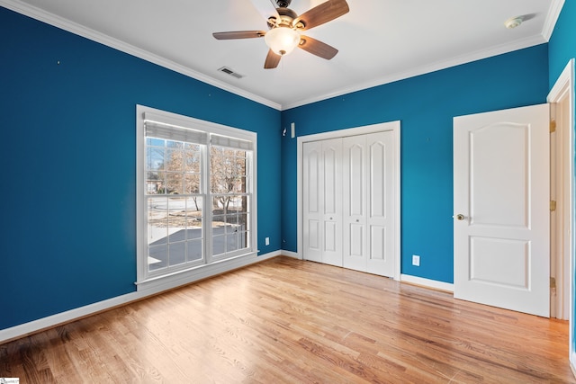 unfurnished bedroom with wood finished floors, visible vents, baseboards, ornamental molding, and a closet