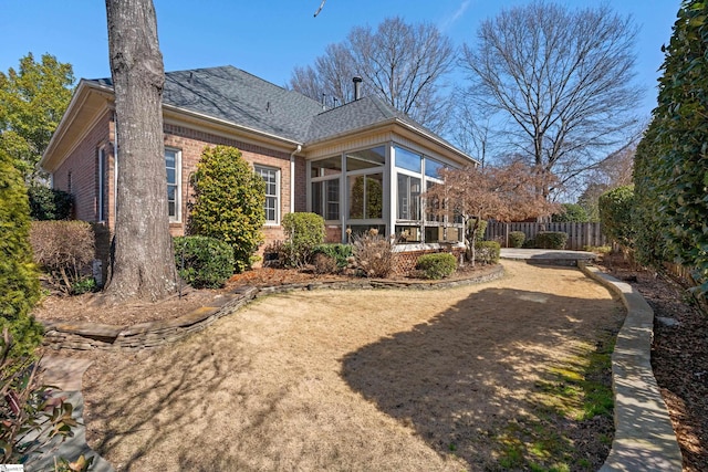 back of property with a shingled roof, a sunroom, brick siding, and fence