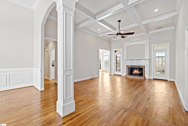 unfurnished living room featuring a brick fireplace, decorative columns, a wealth of natural light, and a ceiling fan