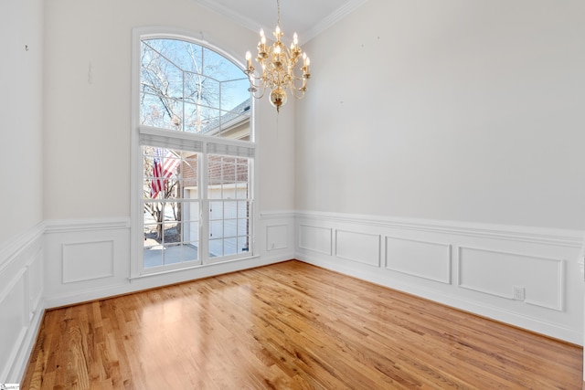 unfurnished dining area featuring a wainscoted wall, ornamental molding, light wood-style flooring, and a notable chandelier