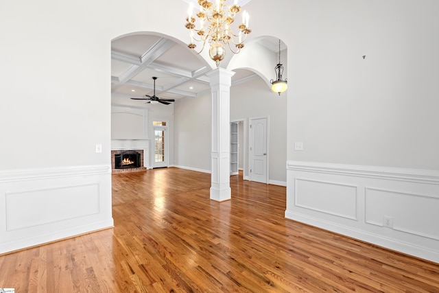 unfurnished living room featuring arched walkways, a fireplace, ceiling fan, coffered ceiling, and ornate columns