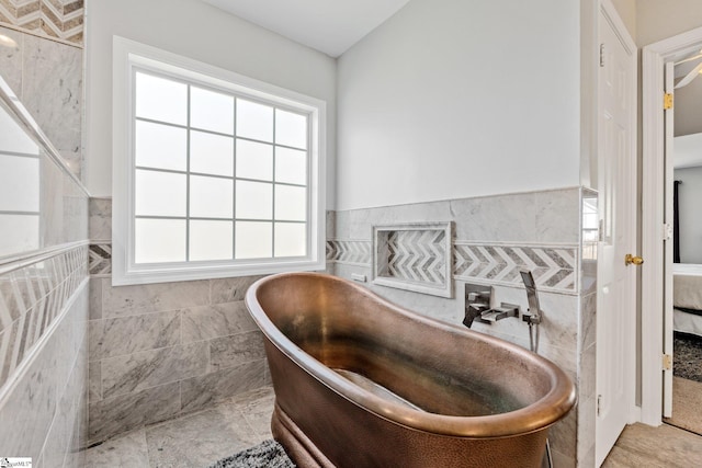 interior space featuring a soaking tub, connected bathroom, tile walls, and a wainscoted wall