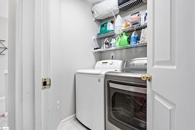 clothes washing area with laundry area, tile patterned flooring, washing machine and clothes dryer, and baseboards