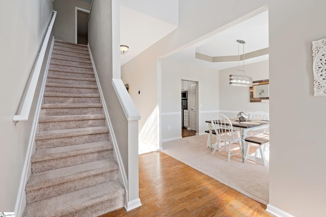 staircase featuring a tray ceiling, wood finished floors, and baseboards