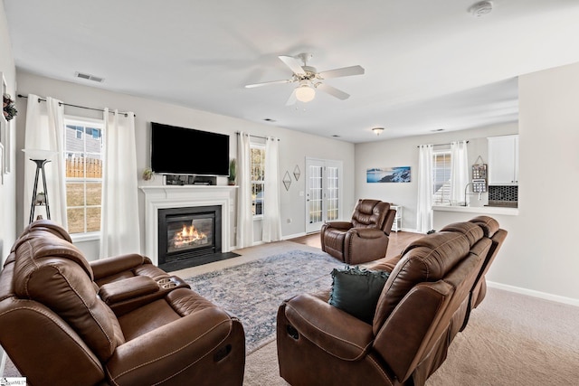 living area featuring a fireplace with flush hearth, a healthy amount of sunlight, visible vents, and baseboards