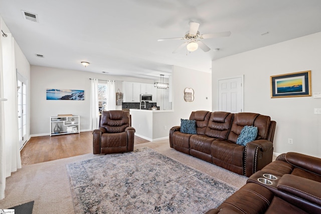 carpeted living area featuring ceiling fan, visible vents, and baseboards