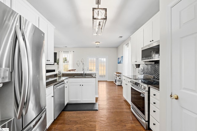 kitchen with dark wood-style floors, stainless steel appliances, backsplash, a sink, and a peninsula