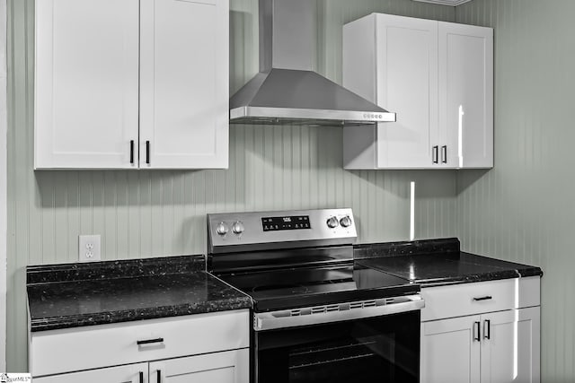 kitchen featuring dark stone counters, wall chimney exhaust hood, stainless steel electric range, and white cabinetry